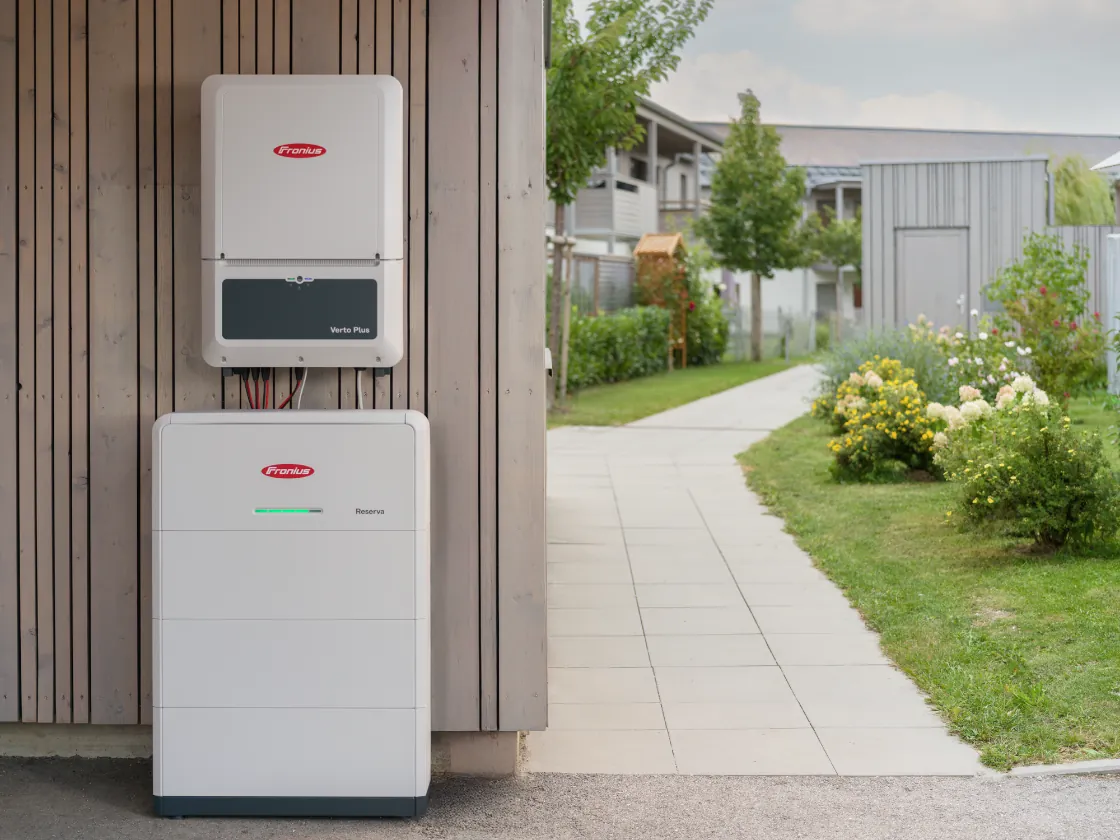 Fronius växelriktare Verto Plus monterad ovanför ett golvstående Fronius Reserva-batteri på en träfasad