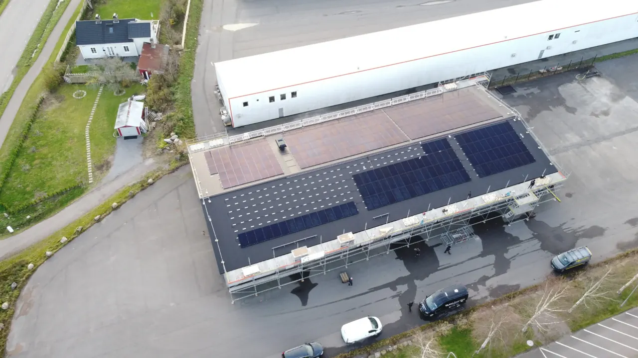 Drönarbild över ett platt företagstak där solpaneler monteras från byggställning